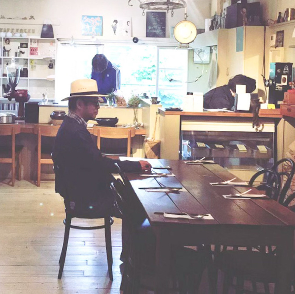 岡本仁氏が木のテーブル席に座る様子